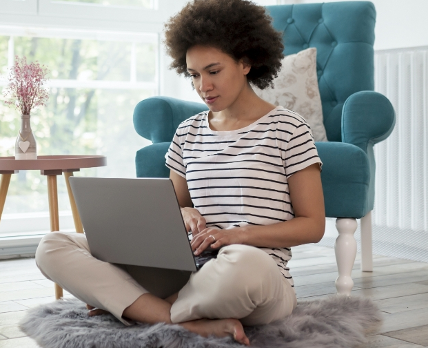A lady in a striped t shirt sitting cross legged on the floor with a laptop on her lap