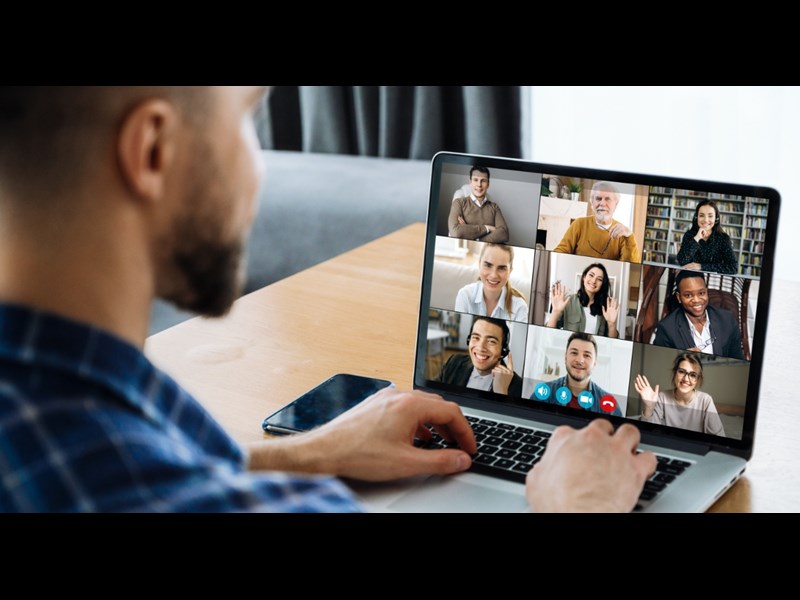 This image showcases a man sitting down in front of his laptop having a virtual meting which has several attendees